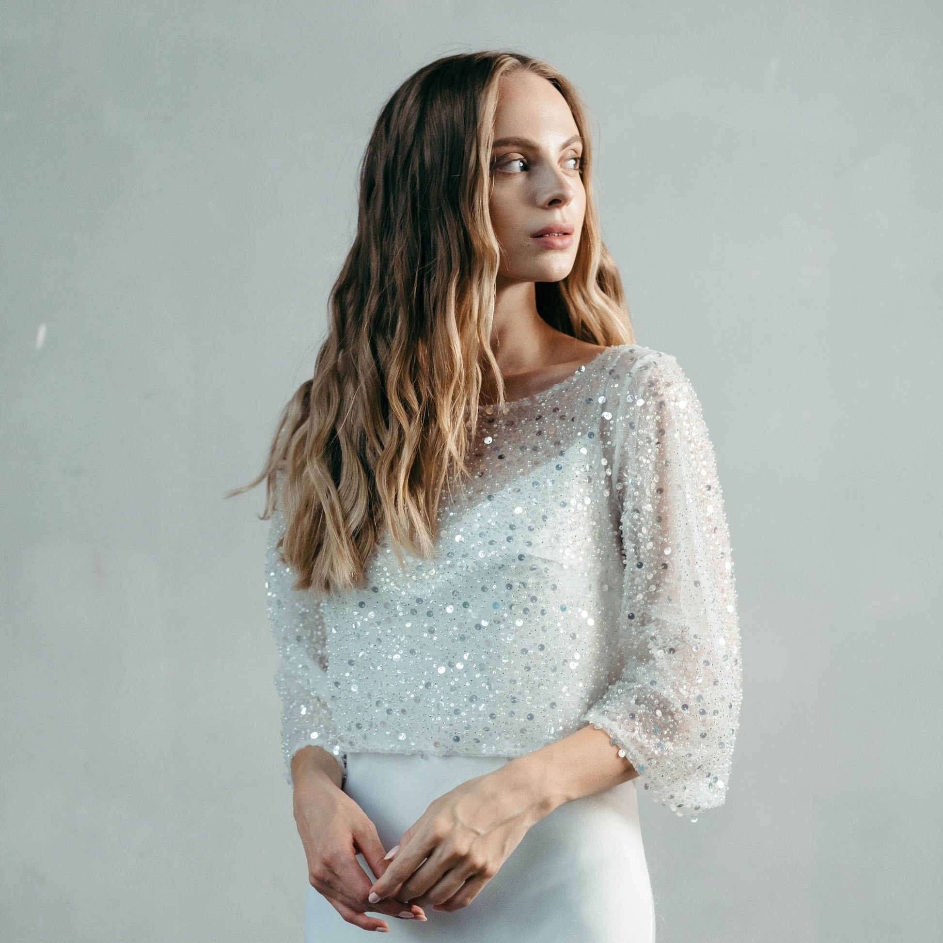 Bride wearing a beaded bridal top with ¾ sleeves and white trousers, styled for a modern civil ceremony or wedding reception.