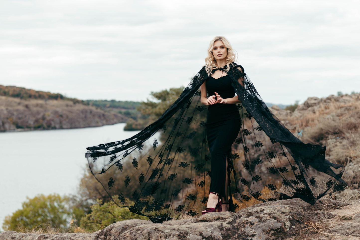 Bride wearing black lace hooded cape with hands raised to veil