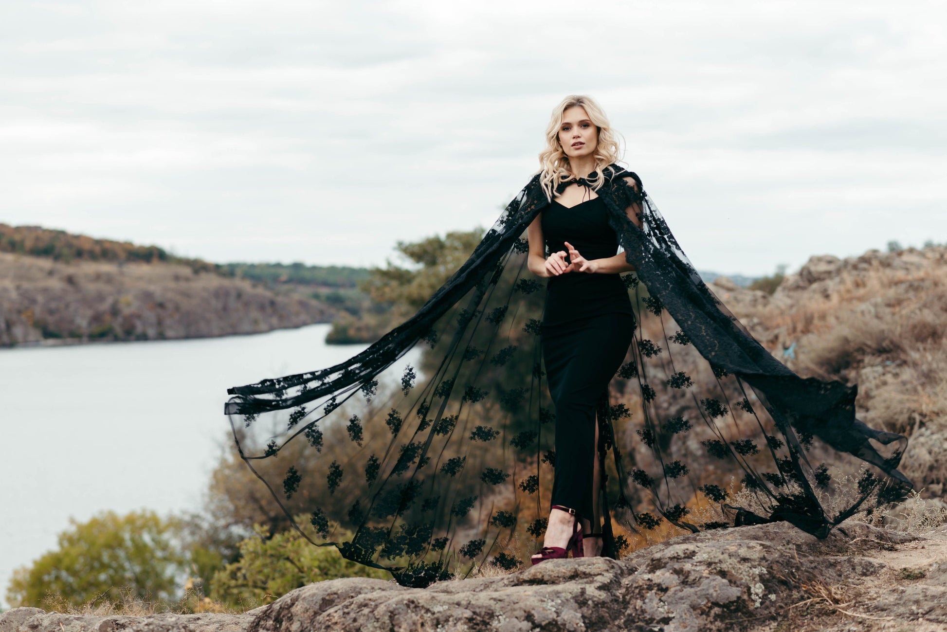 Bride wearing black lace hooded cape with hands raised to veil
