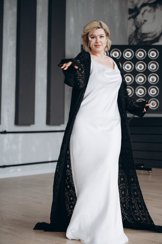 Bride is wearing a simple wedding dress paired with a handmade in the UK black macrame lece bridal cape with sleeves