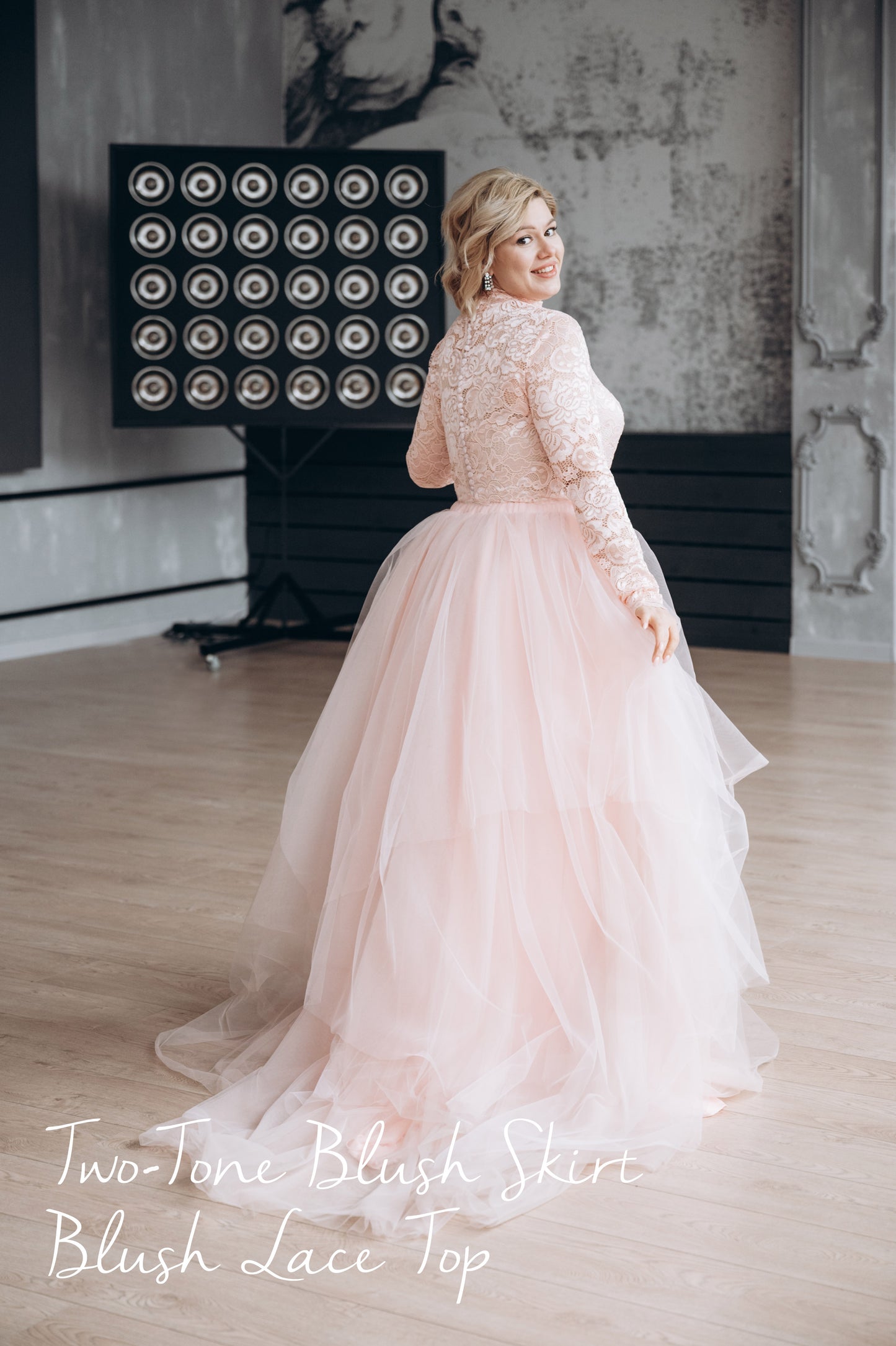 Back view of plus-size bride wearing a blush pink lace top with delicate button-back detail, paired with a flowing ombré pink tulle skirt featuring a soft train—romantic and effortlessly elegant.