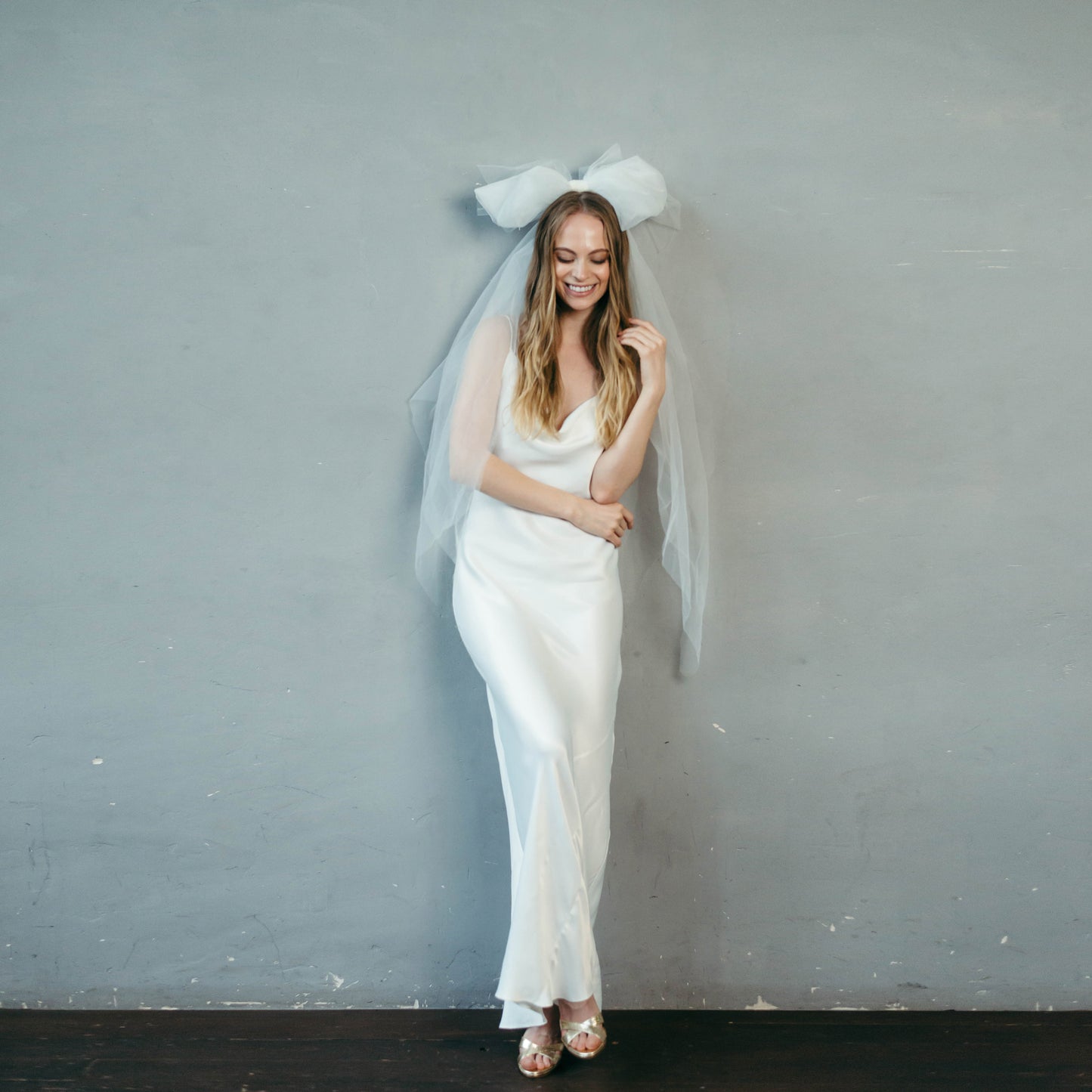 Bride with oversized tulle bow veil styled over satin slip dress, contemporary bridal look.