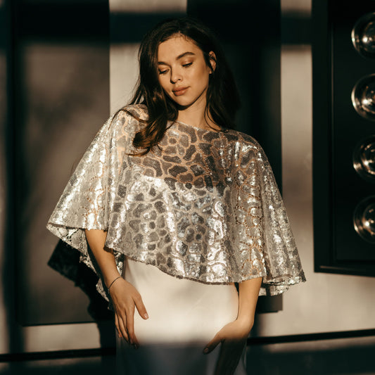 Bride wearing silver sequin bridal capelet over ivory slip dress, modern wedding cover up.