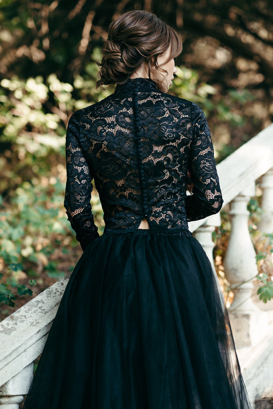 Bride wearing black long-sleeve high-neck lace bridal top with tulle skirt, standing outdoors on stone steps