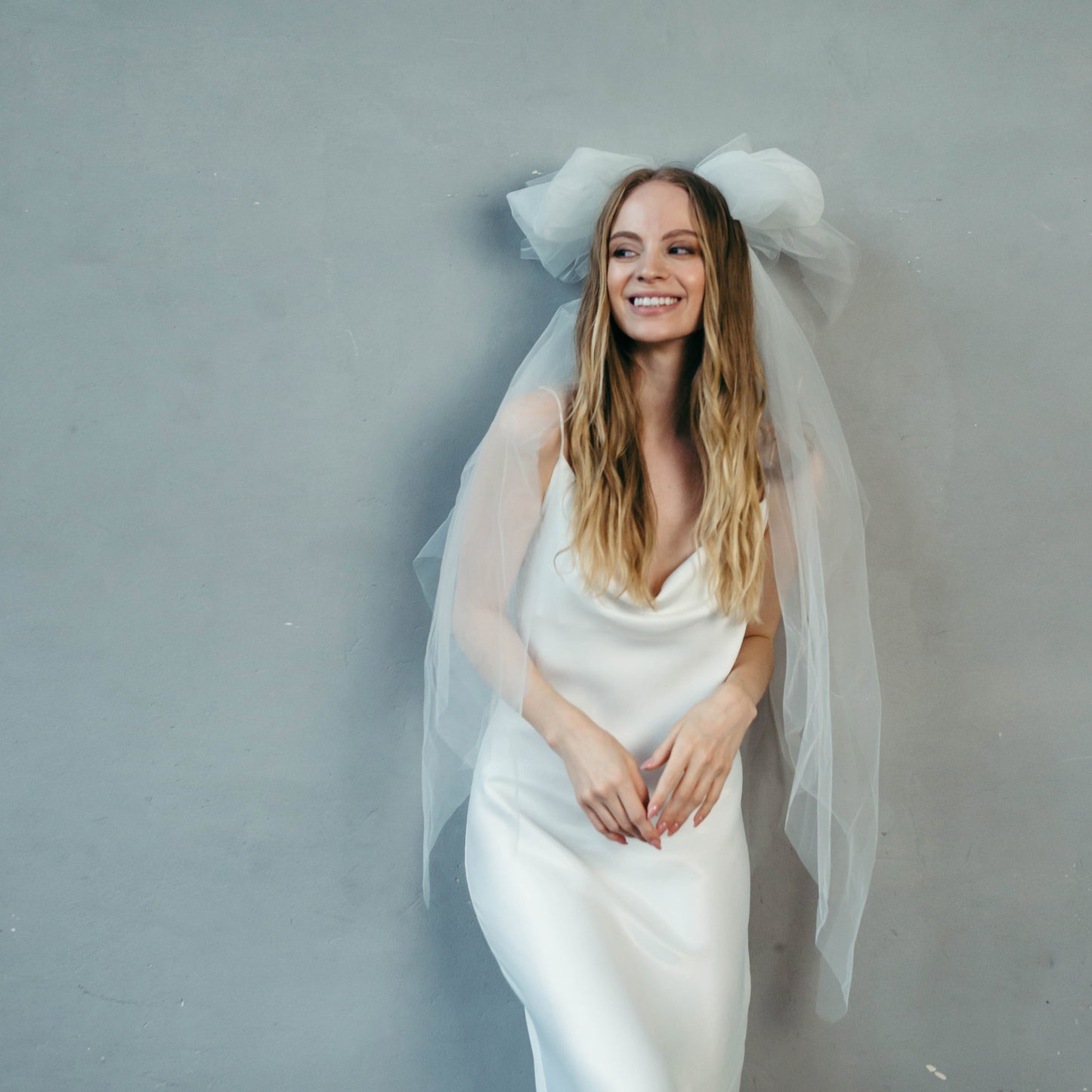 Bride in white satin slip dress with long veil, relaxed modern wedding look.