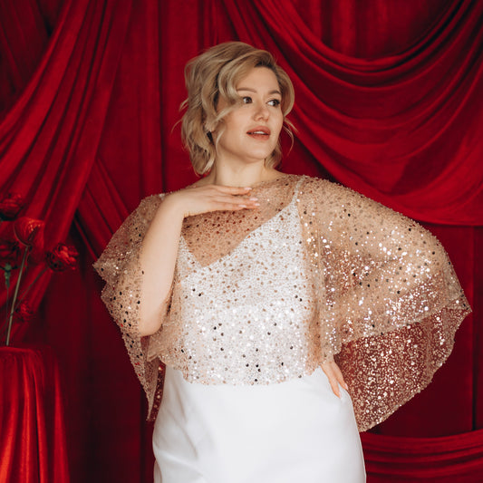 Close-up of bride wearing gold sequin and pearl embellished bridal cape over white gown