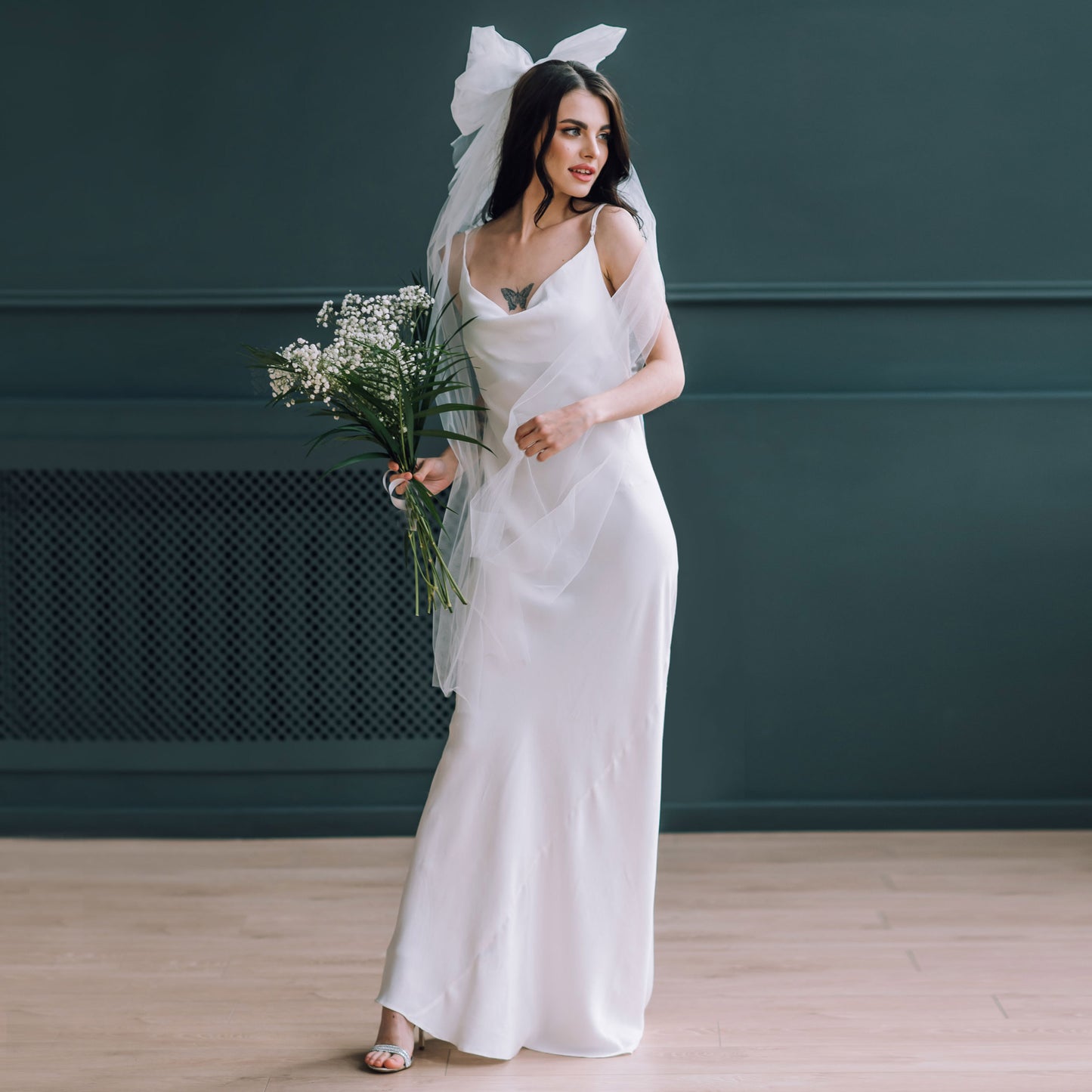 Bride wearing silky satin slip wedding dress with oversized bridal bow veil and bouquet.