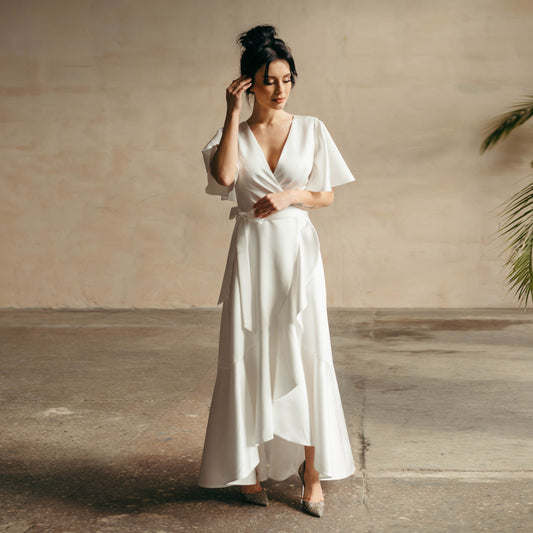 Full-body front view of model wearing ivory satin high-low bridal gown, standing in soft natural light.