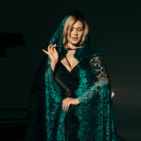 Teal lace bridal cape with hood, worn over a strappy black wedding gown