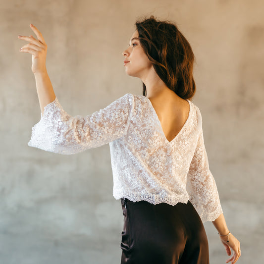 White lace bridal top with floral design and deep V-back, styled with black trousers for a crisp, alternative wedding look.