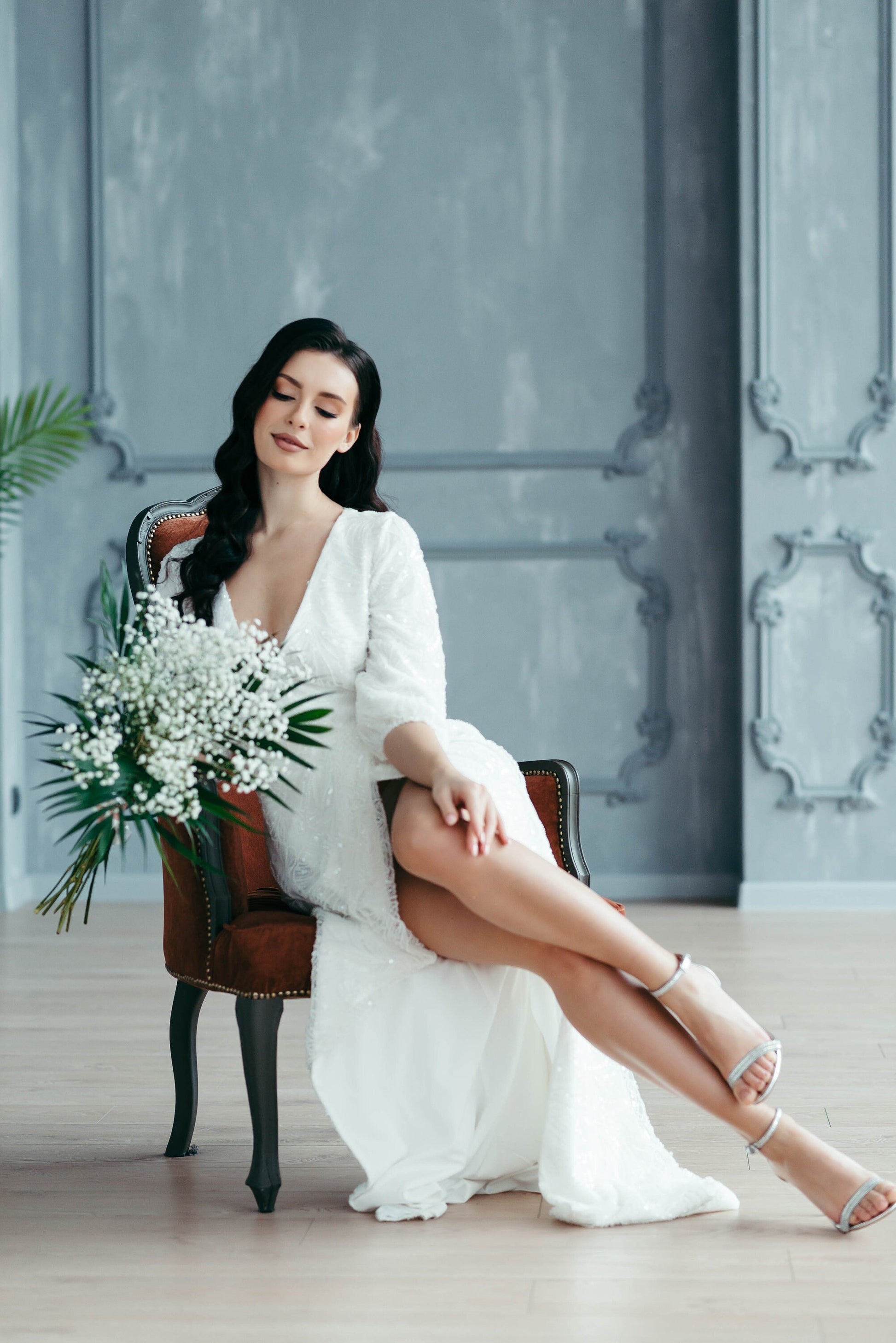 Bride standing holding green bouquet in beaded lace bridal gown with long sleeves