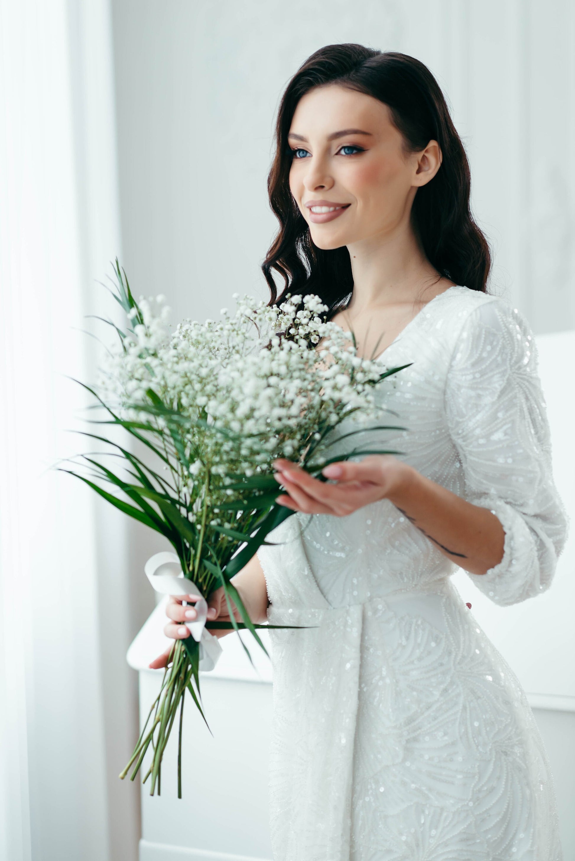 Bride smiling in long-sleeved ivory gown with sequins and front slit
