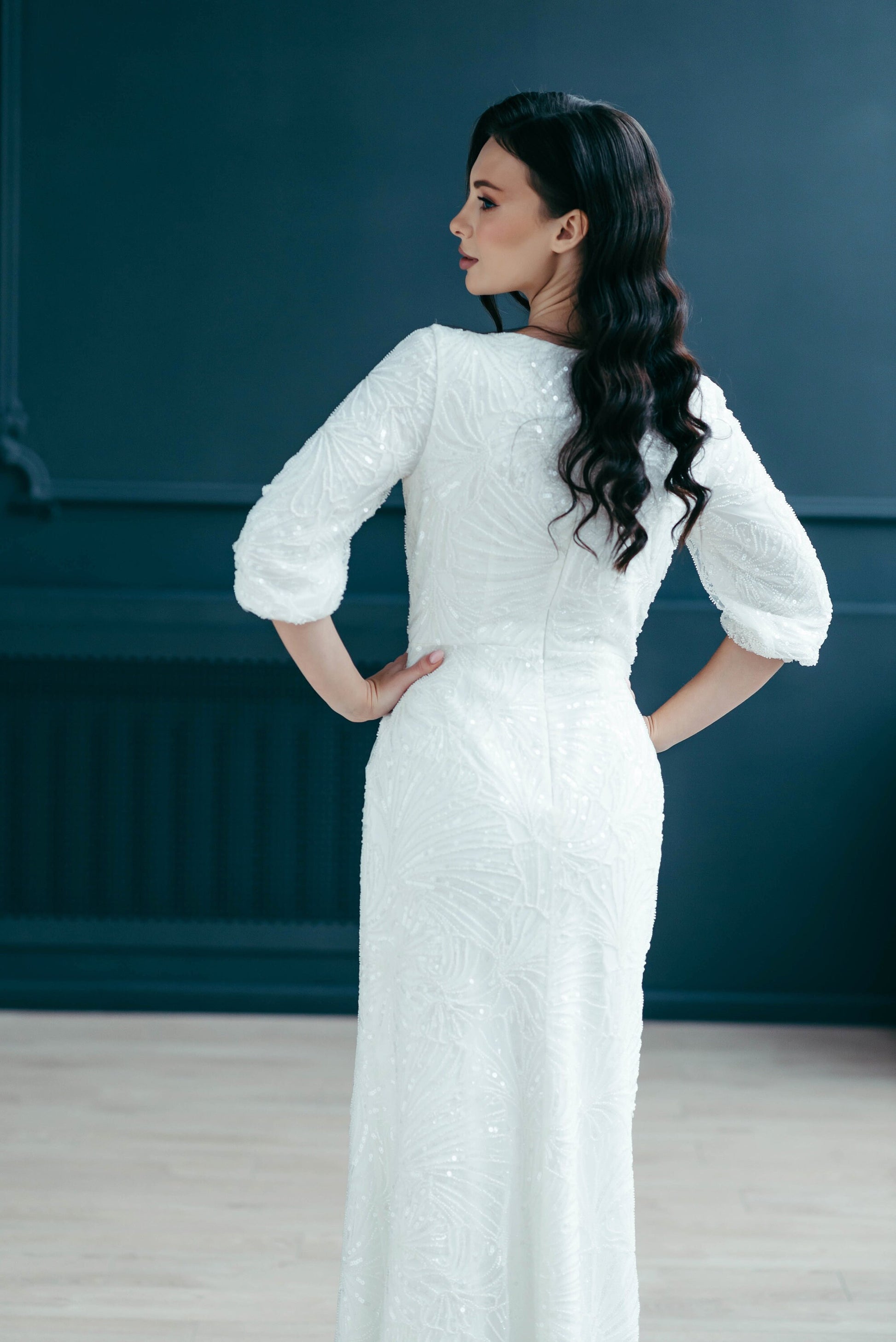 Bride posing sideways in full-length sequin wedding dress with slit and sleeves