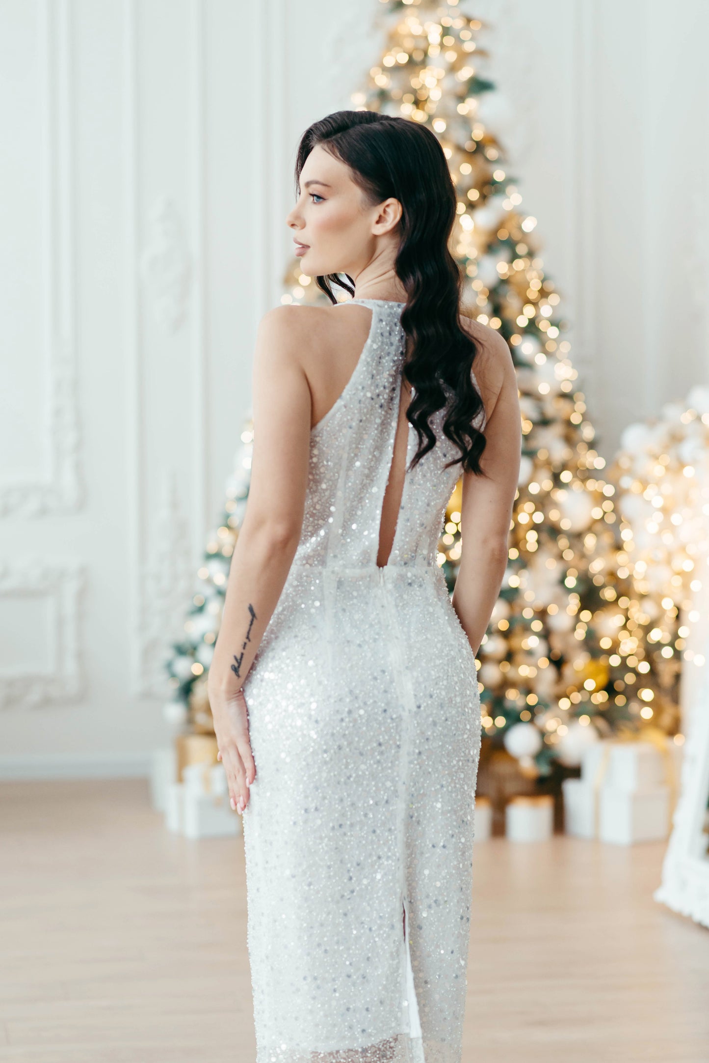 Woman in a silver midi wedding dress standing in front of a decorated Christmas tree.
