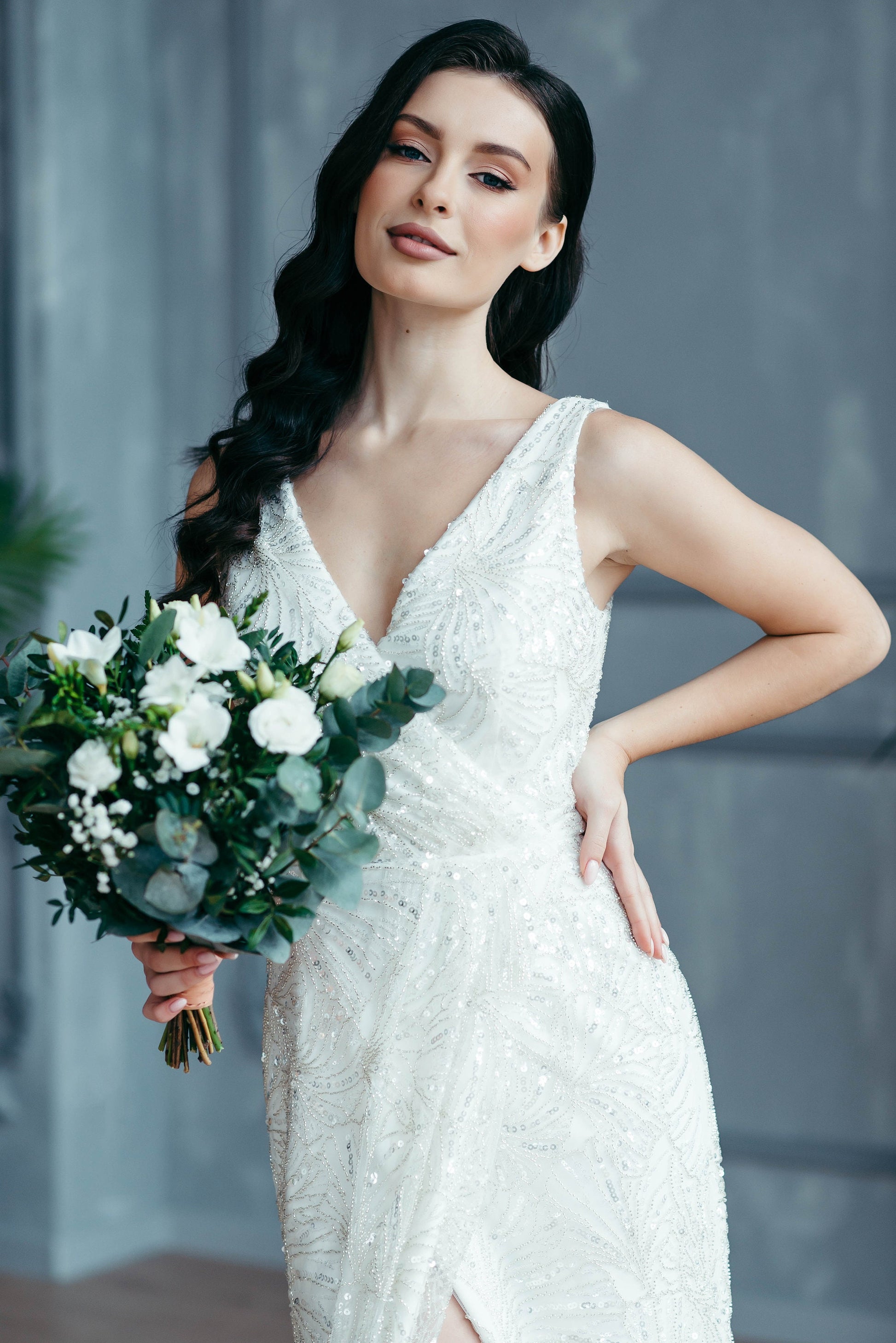 Woman wearing figure-hugging beaded wedding dress, natural makeup, holding bouquet – elegant bridal styling inspiration.
