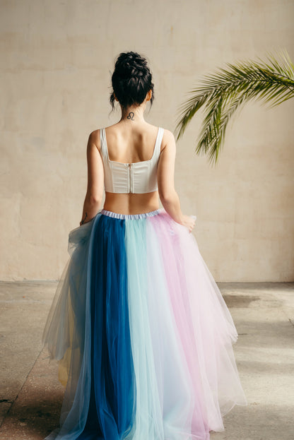 Woman wearing a two-tone tulle wedding skirt with blue and pink gradient, standing against a neutral wall.