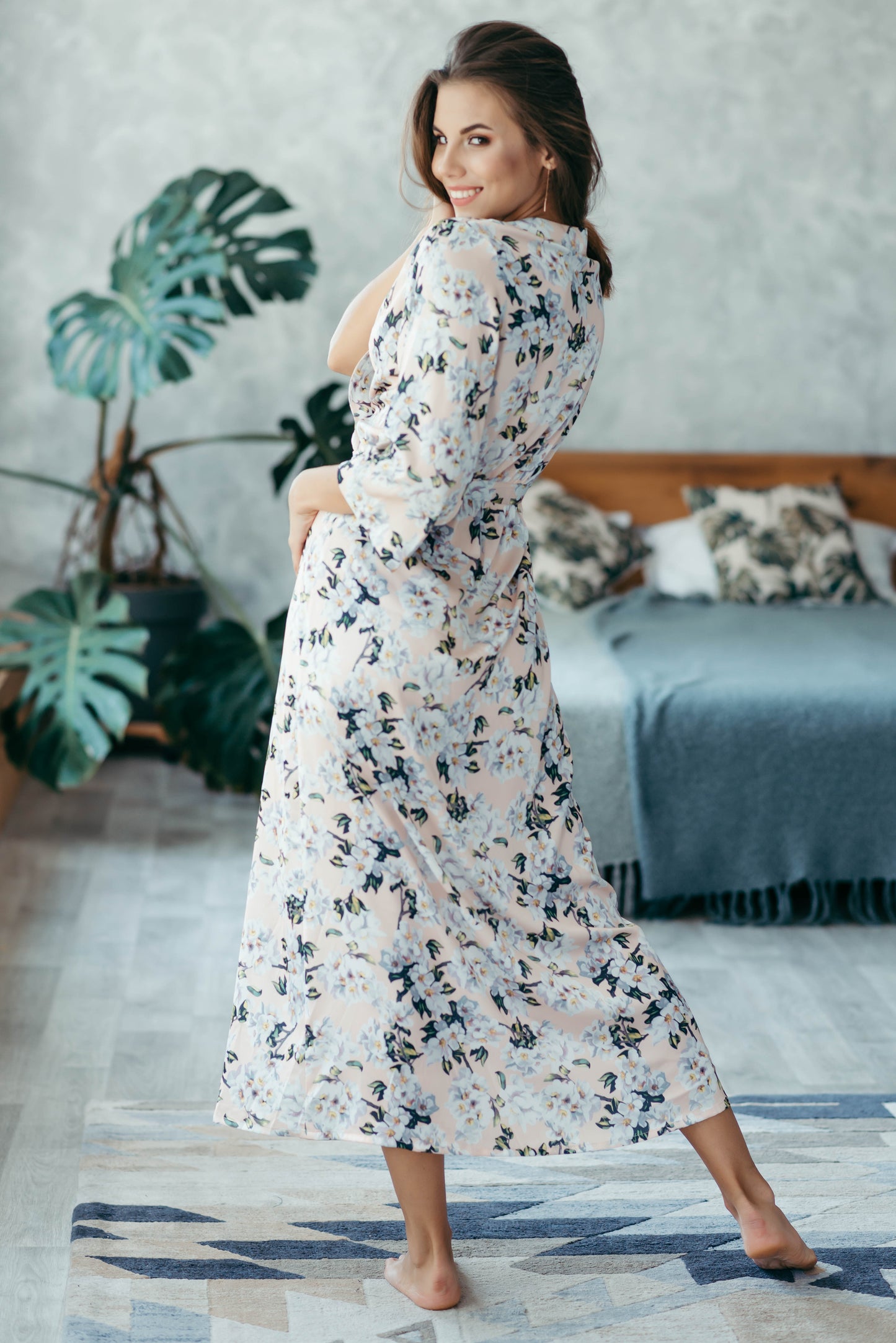 Bride wearing floral satin bridesmaid robe, seated on bed