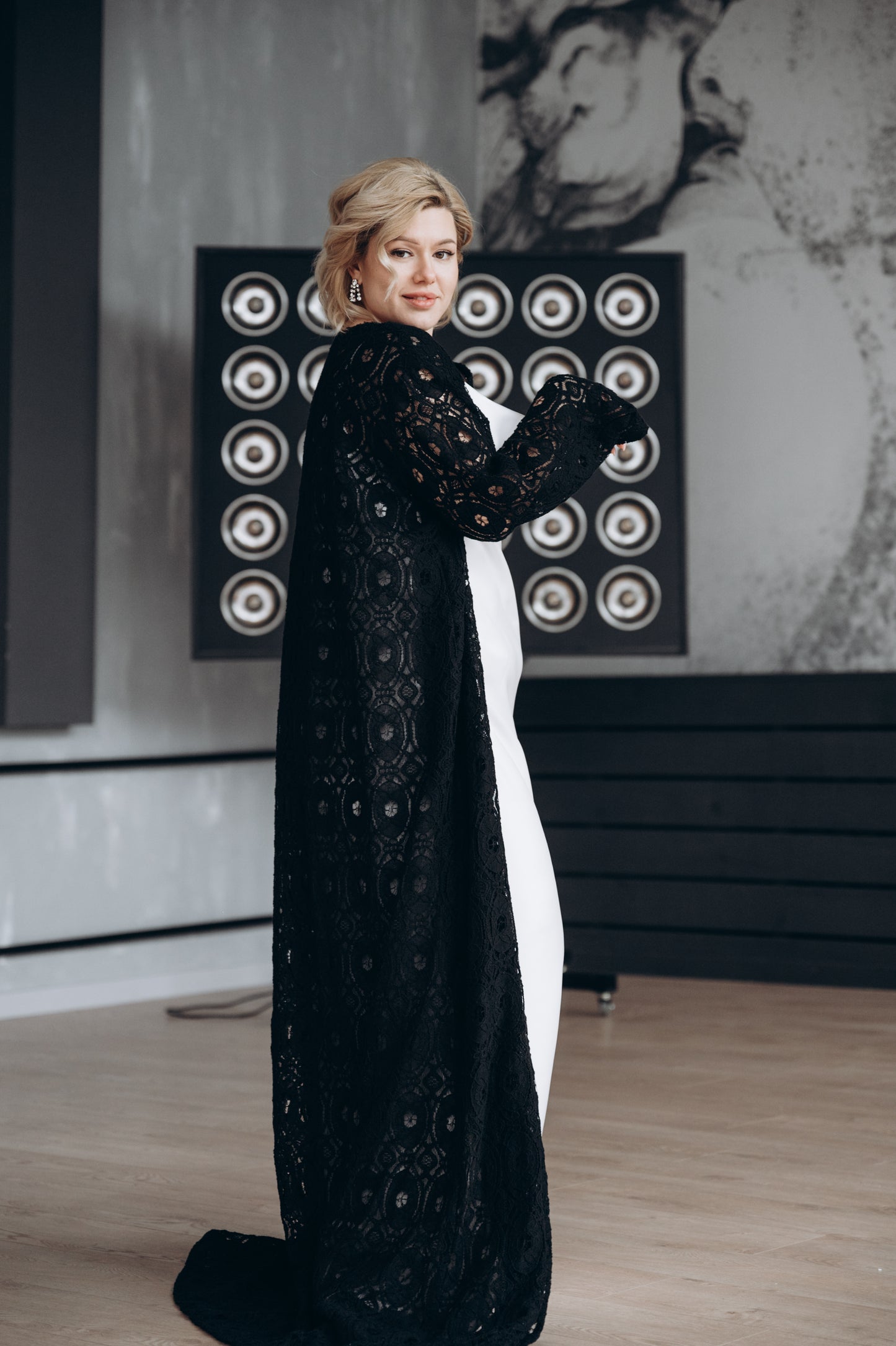 Bride wearing white dress with black macramé lace cape, walking