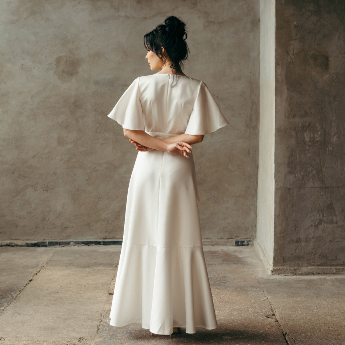 Back view of a simple elopement dress with model standing still, emphasizing skirt length and angel sleeve.