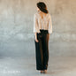 Rear view of cream lace wedding top with black trousers, highlighting the open V-back and scalloped hem.