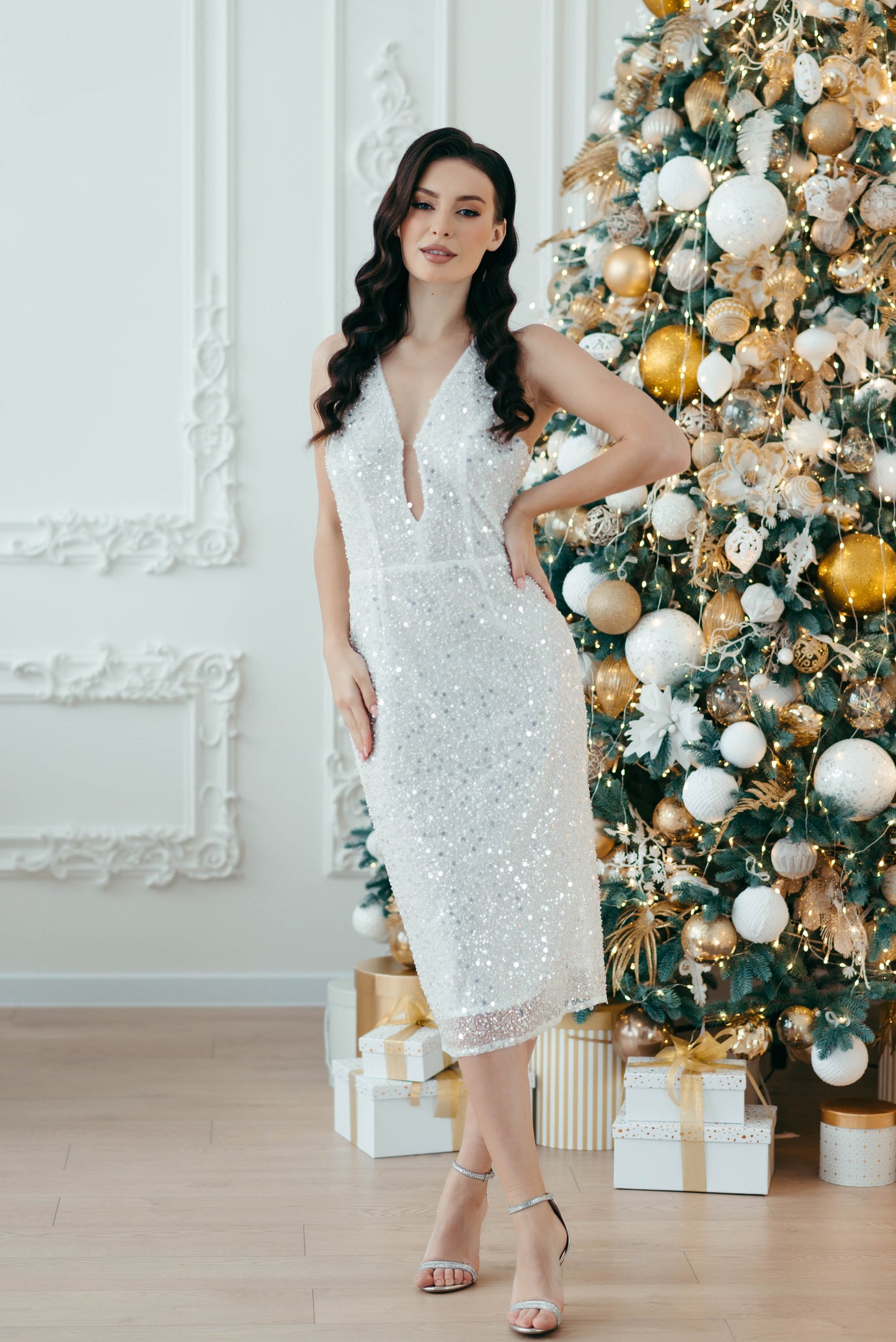 Bridce in a white sequin dress standing in front of a decorated Christmas tree.