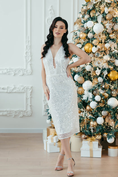 Bridce in a white sequin dress standing in front of a decorated Christmas tree.
