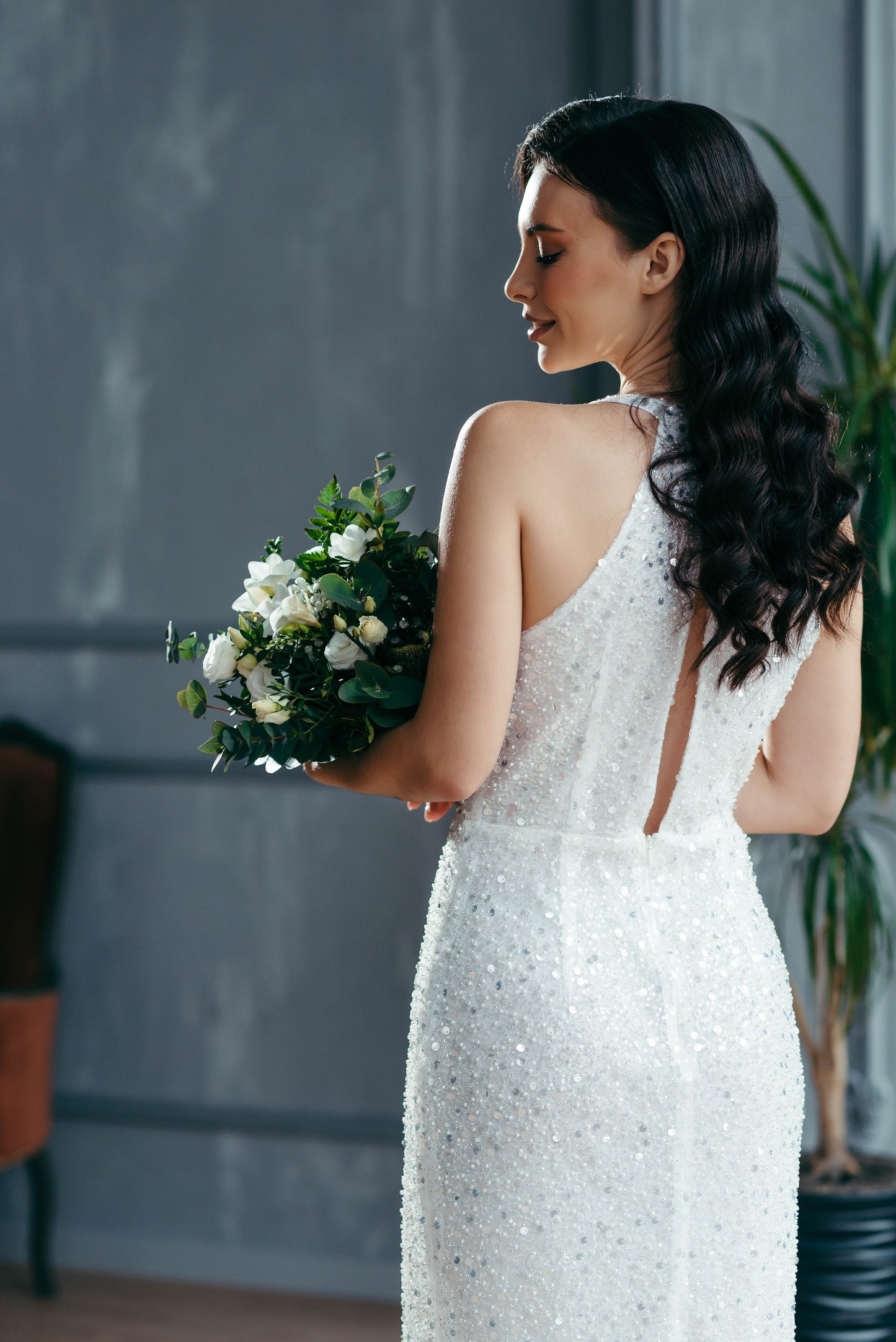 Woman in a white sequined beaded wedding dress holding a bouquet indoors.