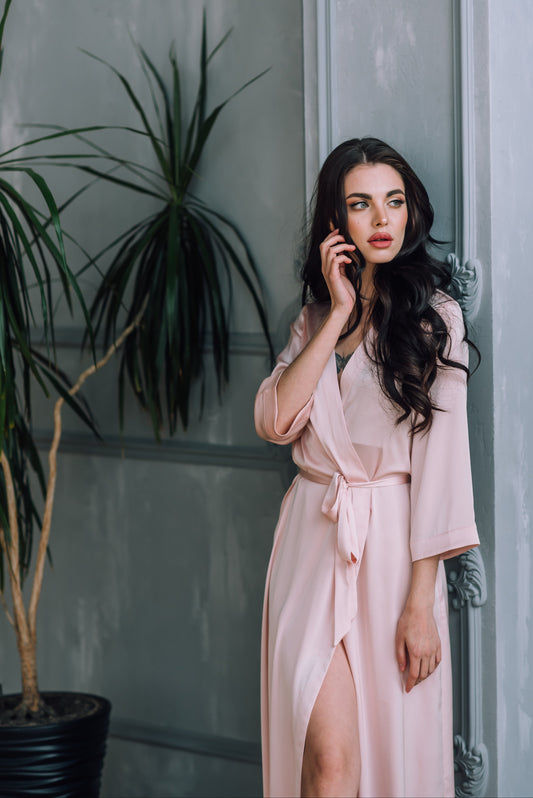 Cute girl relaxing in a blush pink long silky satin dressing gown