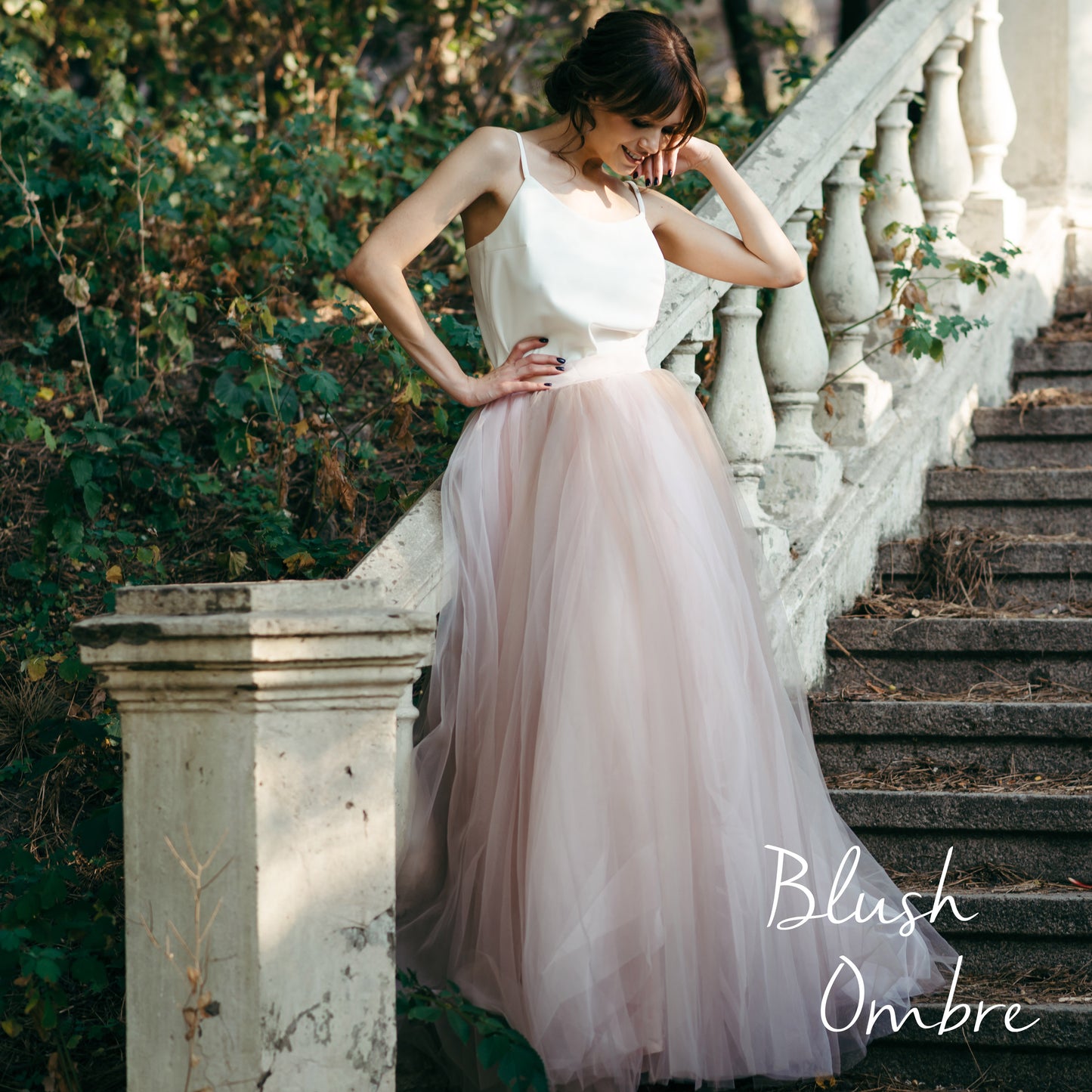 Bride in muted pink and grey ombré wedding skirt in low light on stone staircase