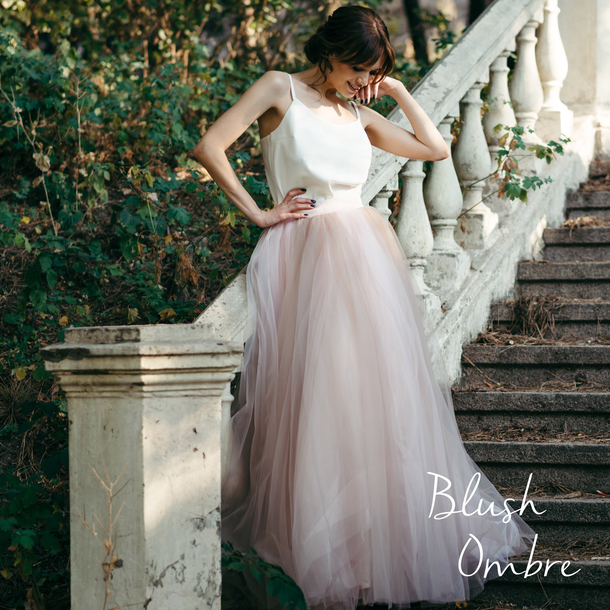 Bride in muted pink and grey ombré wedding skirt in low light on stone staircase