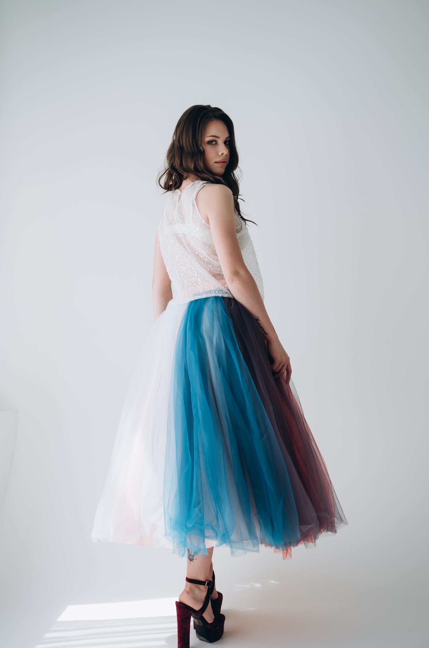 Woman wearing a white top and colorful tulle midi wedding skirt on a white background