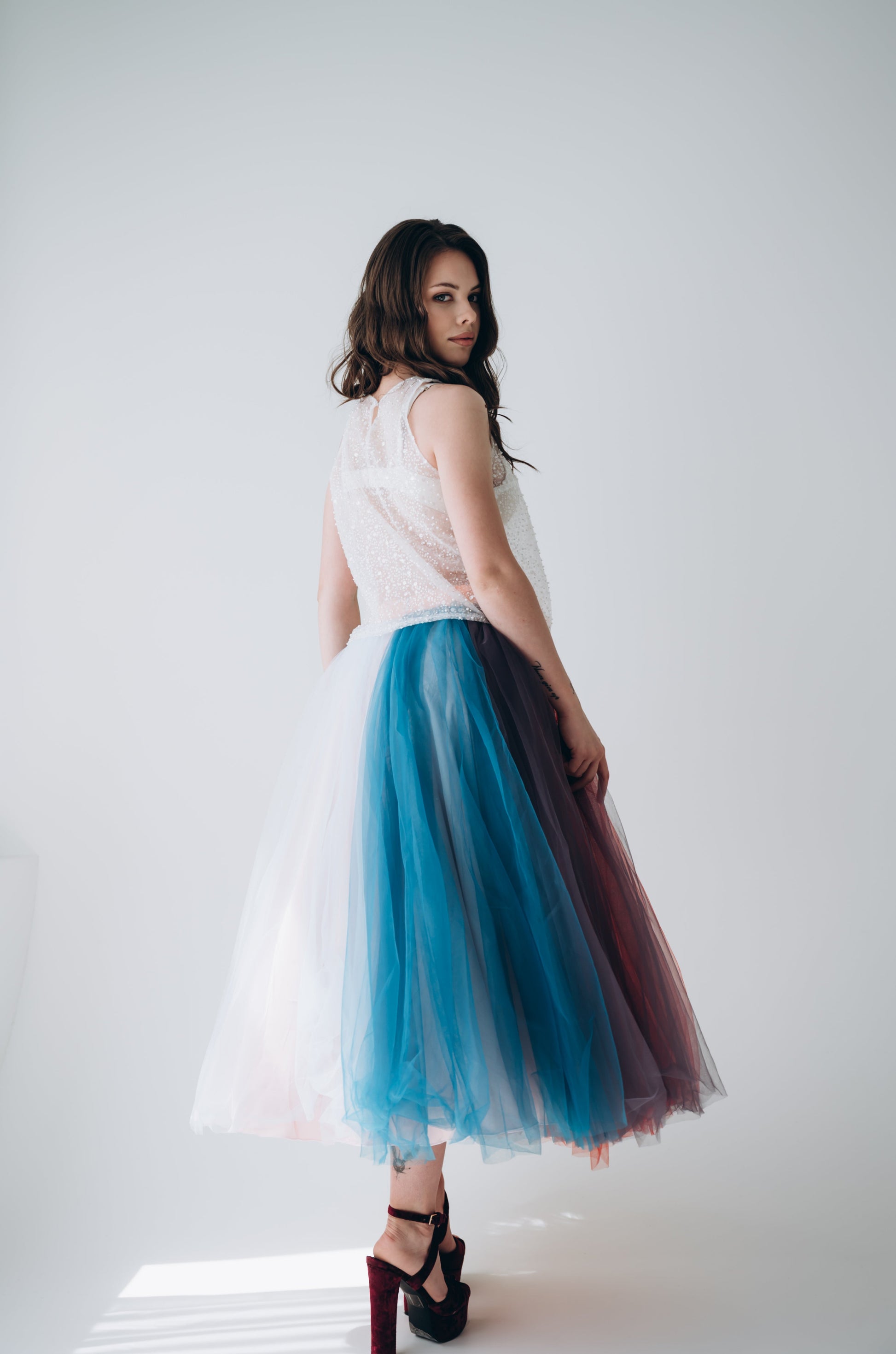 Woman wearing a white top and colorful tulle midi wedding skirt on a white background