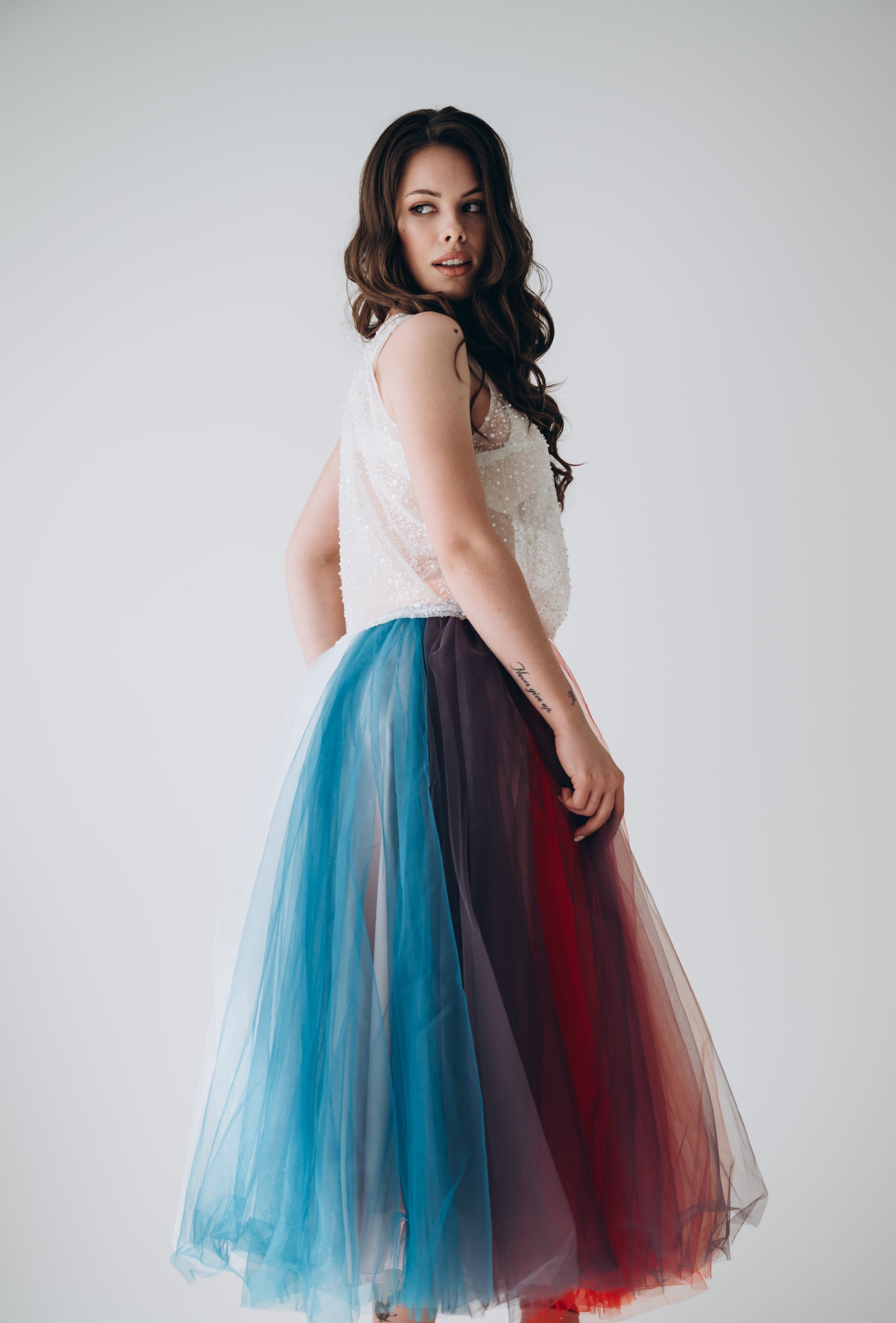 Bride wearing a rainbow tulle skirt with a white top against a plain background
