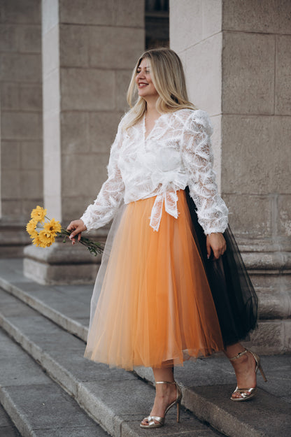 Woman in a white lace top and orange tulle midi skirt standing on steps.