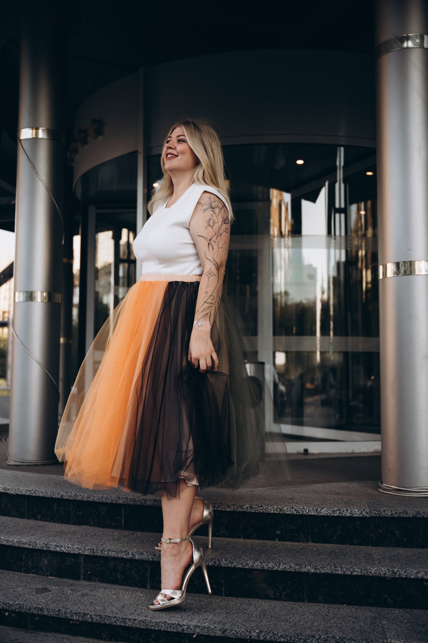 Woman in a white top and layered midi tulle skirt standing on steps of the registry office