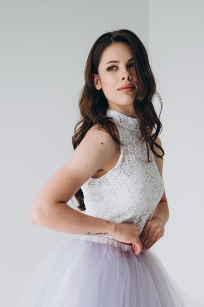 Woman wearing a white lace bridal top and light purple tulle skirt against a plain background