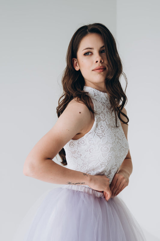 Woman wearing a white lace bridal top and light purple tulle skirt against a plain background