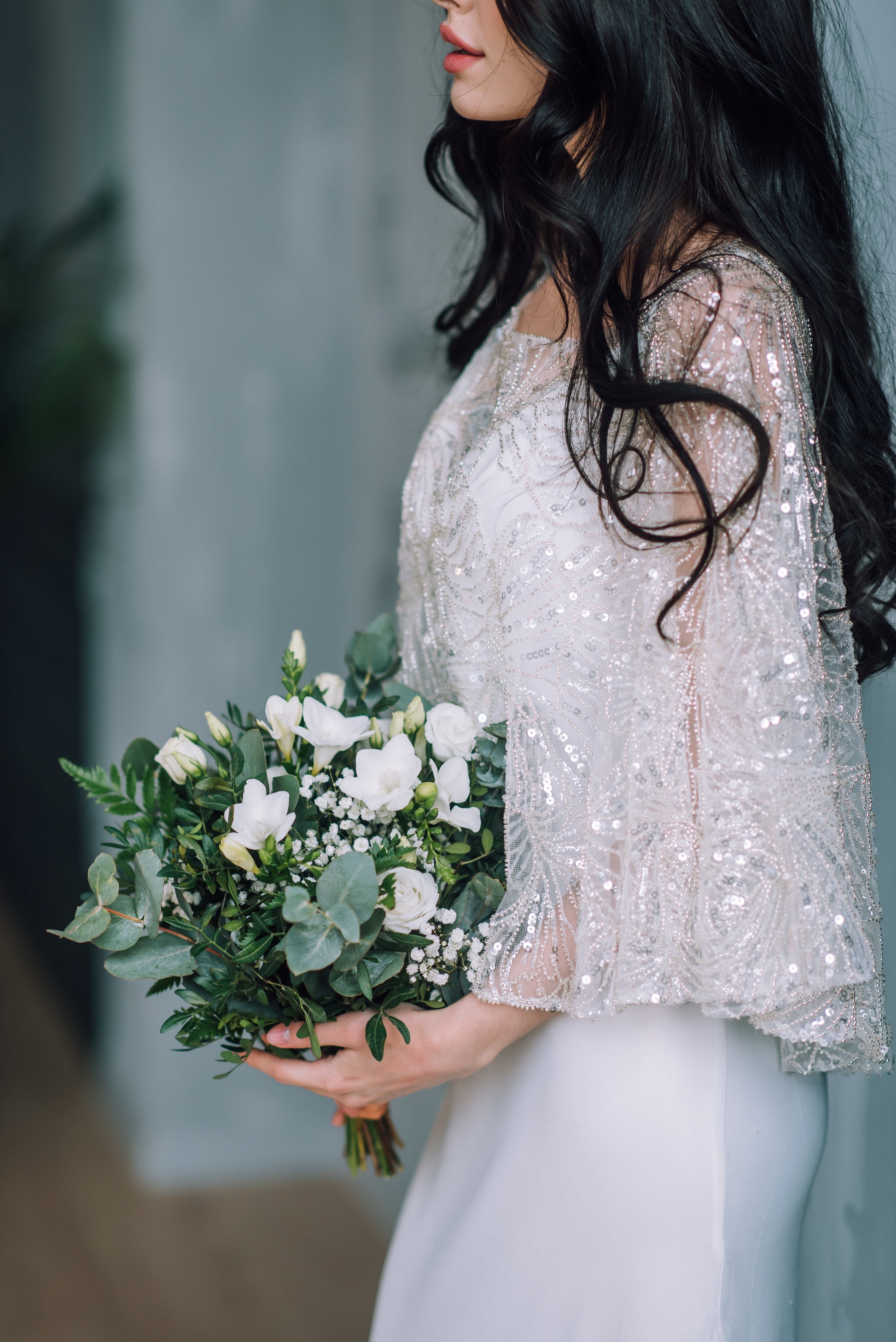 Bride in a sparkly wedding cape holding a bouquet of flowers against a blurred background