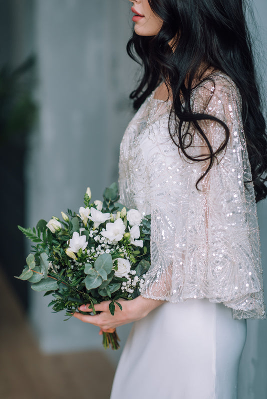 Bride in a sparkly wedding cape holding a bouquet of flowers against a blurred background
